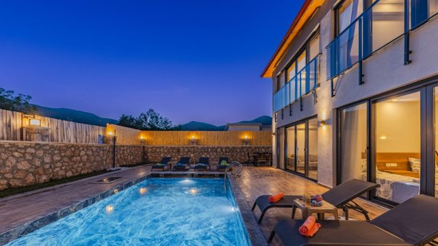 Luxurious villa with pool lit at twilight, available with a booking deposit